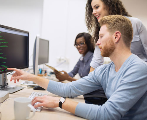 QA Engineer Skills (man and two women pointing at computer screen next to desk in discussion)