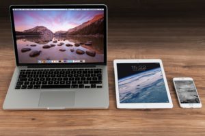 What is Quality Assurance Testing (picture shows a wood desk with a Macbook laptop, an iPad, and an iPhone on it)