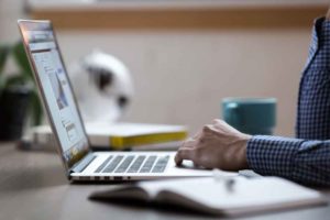 Bug Report Best Practices (picture shows a desk with a coffee cup and a laptop, and a person's hand on the laptop trackpad)