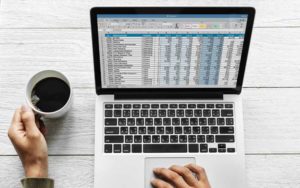 Best Practices for Reporting Bugs (picture shows a hand holding a coffee cup on a desk, and another hand resting on a laptop trackpad)