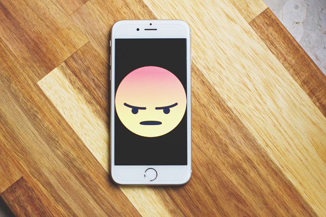 An iPhone on a table with a screen depicting an angry cartoon face to represent bad user experience