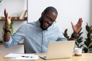 QA Manager (Black man with glasses staring happily at laptop on desk)