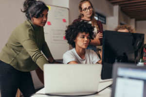 How to Be a Good QA Manager (three women sitting in front of a laptop discussing QA testing)